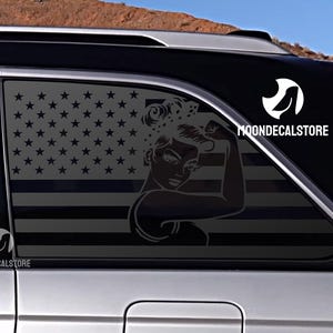May include: A black decal featuring the American flag with a silhouette of a woman flexing her bicep. The decal is on a car window. The text "MOONDECALSTORE" is visible.