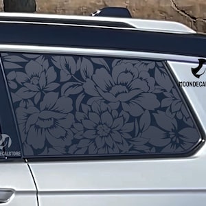 May include: A gray car window with a floral pattern decal. The decal features a repeating pattern of gray flowers on a gray background. The decal is applied to the back window of the car. The decal has the text "MOONDECALSTORE" on the bottom right corner.