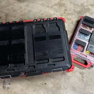 May include: Two black and red toolboxes are shown. The larger toolbox is closed, while the smaller one is open, revealing compartments filled with various hardware items. Both toolboxes have black panels and red accents.