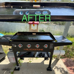 May include: Black Blackstone flat top grill with four burners and a side shelf. The grill has a black finish and orange knobs. The grill is on a stand with wheels. The grill is level and ready to cook.
