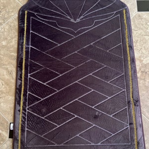 May include: A purple prayer rug with a geometric pattern and gold trim. The rug has a fringed edge and a decorative design at the top.
