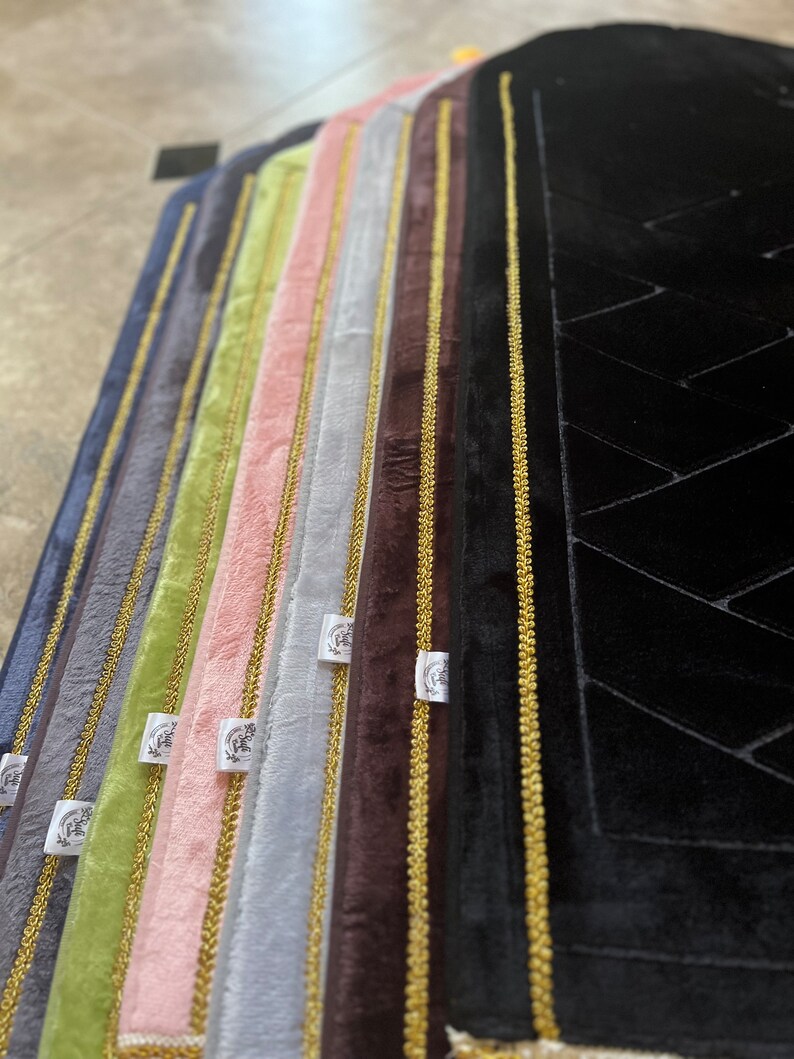 May include: A set of eight prayer rugs with gold trim and a variety of colors, including black, gray, brown, pink, green, and blue. The rugs have a soft, plush texture and are perfect for prayer or meditation.