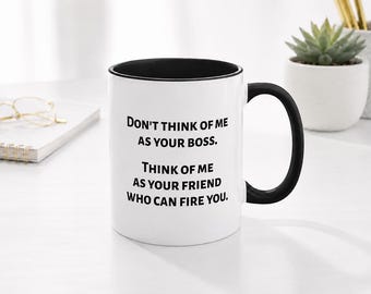 May include: A white ceramic mug with a black interior and a black handle. The front of the mug features black printed text that reads: Don't think of me as your boss. Think of me as your friend who can fire you. The mug has a smooth, cylindrical shape.