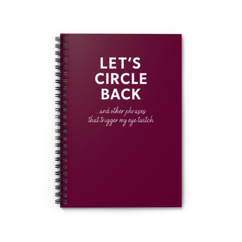 May include: A spiral-bound notebook with a deep burgundy cover. The cover features the text "LET'S CIRCLE BACK" in large white letters, with the phrase "...and other phrases that trigger my eye twitch" below.