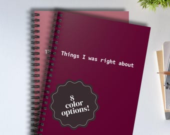 Puede incluir: Un cuaderno de espiral color magenta oscuro con el texto blanco "Things I was right about" impreso en la portada. Una insignia negra festoneada con el texto blanco "8 color options!" está centrada en la parte inferior de la portada.