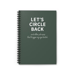 May include: A spiral-bound notebook with a dark green cover. The cover features the text "LET'S CIRCLE BACK" in large white letters, with the phrase "...and other phrases that trigger my eye twitch" below in a smaller, cursive font.