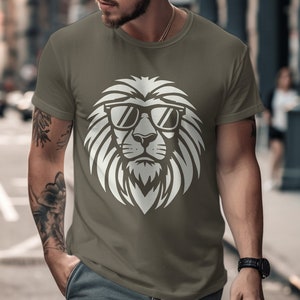 Pode incluir: Camiseta verde-oliva com um desenho gráfico branco de um leão usando óculos de sol. O rosto do leão é o elemento central, com detalhes de pelo e óculos de sol. A camiseta tem mangas curtas e gola redonda.