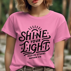 Puede incluir: Camiseta rosa con un gráfico negro que dice "Shine Your Light" e "Inspire Others Matthew 5:16".