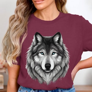 May include: A maroon t-shirt with a graphic of a wolf's face. The wolf has gray fur, blue eyes, and a black nose.