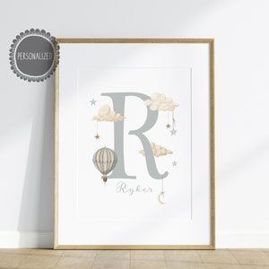 May include: A grey letter R with clouds, stars, and a hot air balloon hanging from the clouds. The name Ryker is written below the letter.