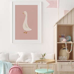 May include: A white goose illustration on a pink background in a white frame. The goose is facing left and has a long neck. The illustration is in a child's room with a wooden shelf and a pink backpack.