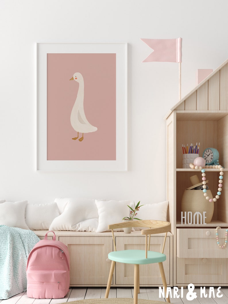 May include: A white goose illustration on a pink background in a white frame. The goose is facing left and has a long neck. The illustration is in a child's room with a wooden shelf and a pink backpack.