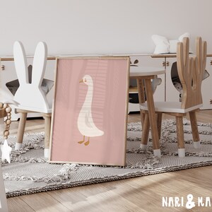 May include: A pink and white children's poster featuring a cartoon goose with a pink background. The poster is leaning against a white bunny-shaped chair in a playroom setting.