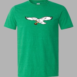 May include: Green t-shirt with a white eagle graphic, detailed with black, holding a brown football. The eagle is depicted mid-flight. The t-shirt is a solid green colour.