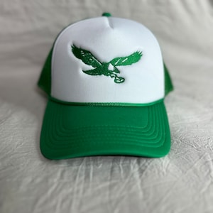 May include: A green and white trucker hat with an embroidered green eagle on the front.