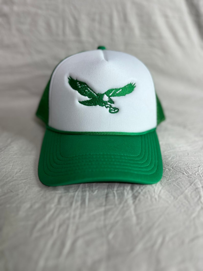 May include: A green and white trucker hat with an embroidered green eagle on the front.