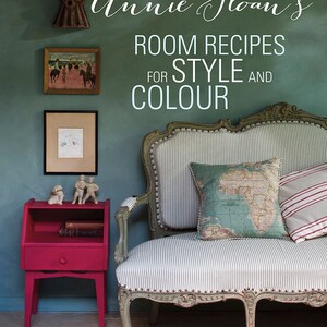 May include: A teal green wall with a vintage style sofa with a striped fabric and a map patterned pillow. A small pink side table with a book and two figurines sits in the corner of the room. The text "Annie Sloan's Room Recipes for Style and Colour" is written in white on the wall.