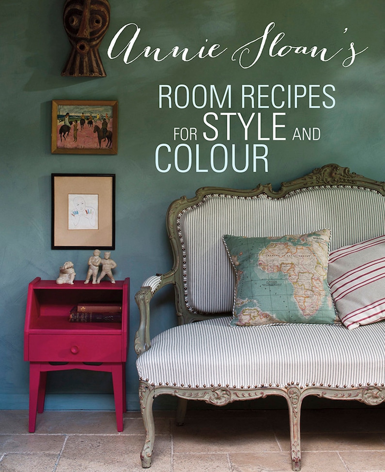 May include: A teal green wall with a vintage style sofa with a striped fabric and a map patterned pillow. A small pink side table with a book and two figurines sits in the corner of the room. The text "Annie Sloan's Room Recipes for Style and Colour" is written in white on the wall.