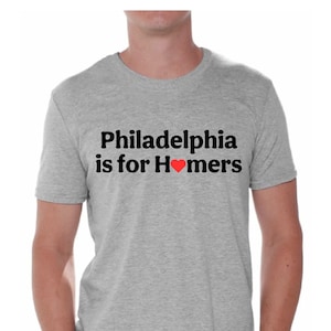 May include: A gray t-shirt with the text "Philadelphia is for Homers" in black with a red heart in place of the "o" in "Homers".