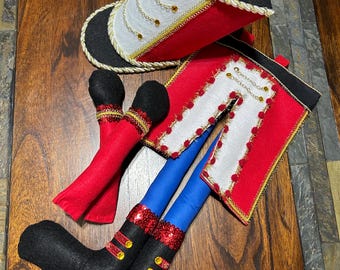 May include: A felt toy nutcracker doll with red and white uniform, blue legs, black boots, and a black and white hat.