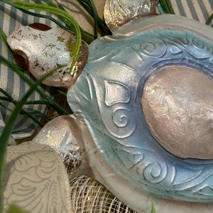 May include: A blue and white ceramic turtle with a silver finish. The turtle has a detailed design on its shell and is decorated with a silver glitter finish.