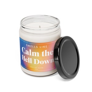 Pode incluir: Uma vela branca de mistura de soja num frasco de vidro transparente com tampa preta. O rótulo apresenta o texto "Smells Like Calm the Hell Down" em branco sobre um gradiente de azul, laranja e rosa. A vela tem 255 gramas.