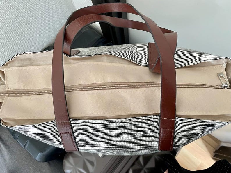 以下が含まれることがあります： 茶色の革のハンドルとジッパーの留め具が付いた、ストライプのキャンバス地のトートバッグ。丈夫な素材で作られており、広々とした内装です。