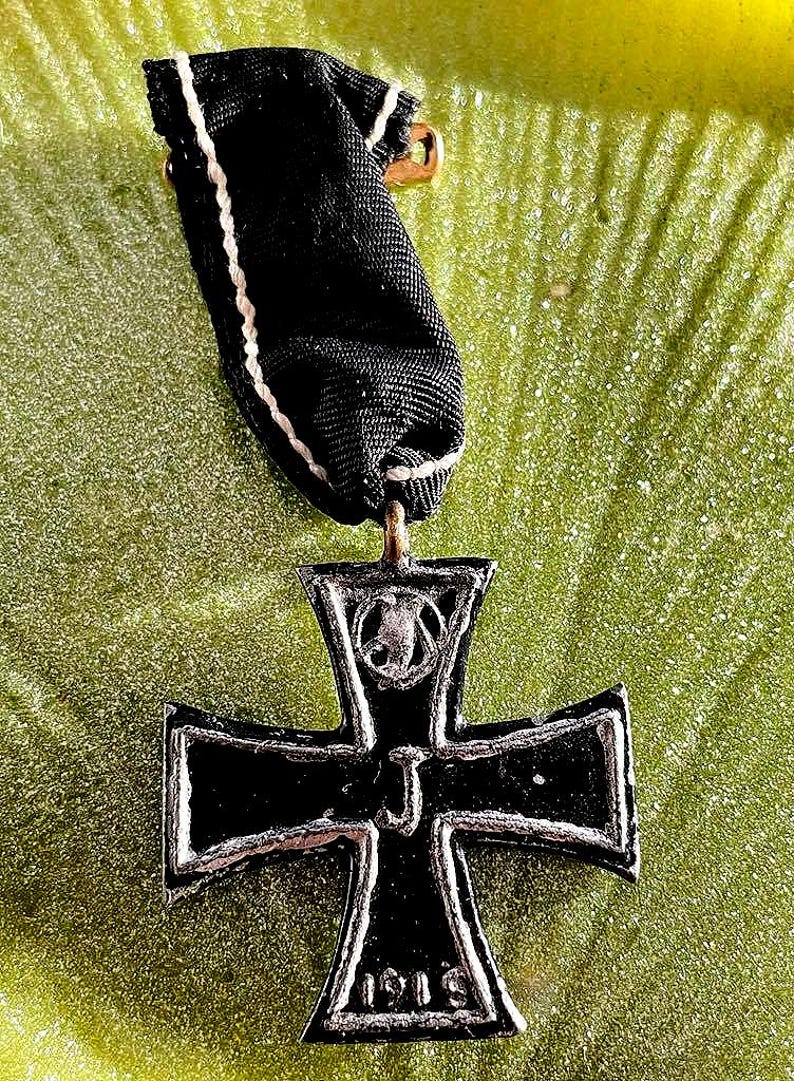 May include: A black Iron Cross medal with a silver border and a black ribbon. The medal has the year 1914 on the bottom and the letter "J" in the centre. The ribbon is black with white trim.