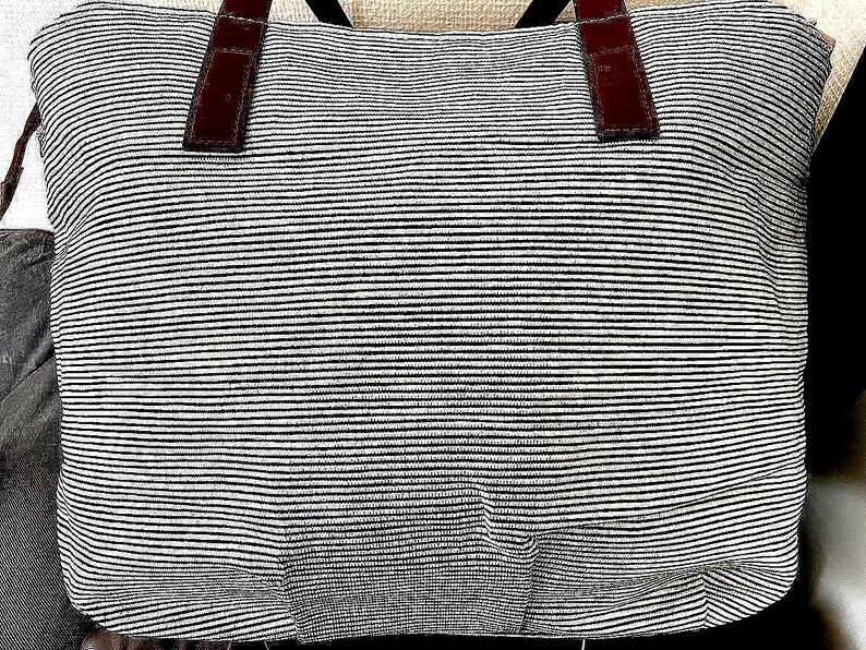 以下が含まれることがあります： 黒と白のストライプのトートバッグで、茶色の革のハンドルが付いています。