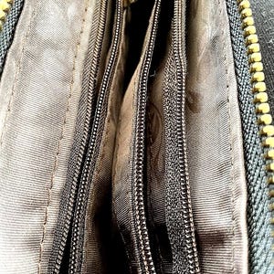 Peut inclure: Gros plan sur l'int&eacute;rieur d'un portefeuille gris fonc&eacute; avec plusieurs compartiments zipp&eacute;s. Les fermetures &eacute;clair sont noires avec des tirettes en m&eacute;tal dor&eacute;. La doublure est en tissu gris clair.