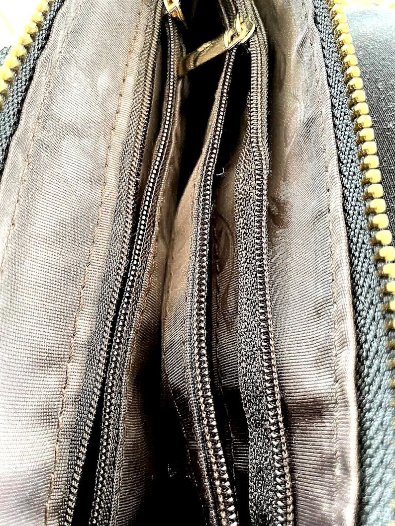 Peut inclure: Gros plan sur l'int&eacute;rieur d'un portefeuille gris fonc&eacute; avec plusieurs compartiments zipp&eacute;s. Les fermetures &eacute;clair sont noires avec des tirettes en m&eacute;tal dor&eacute;. La doublure est en tissu gris clair.