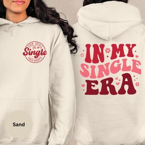 May include: A white hoodie with a red and pink graphic on the front that says "Yep, Still Single and Happy" and a red and pink graphic on the back that says "In My Single Era".