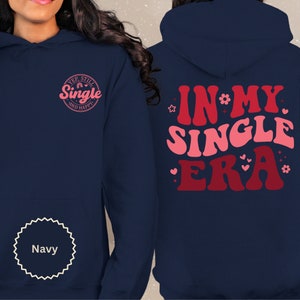 May include: Navy blue hoodie with a pink and red graphic on the back that says "In My Single Era" and a pink graphic on the front that says "Yep, Still Single and Happy".