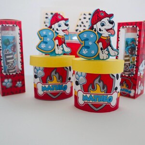 Puede incluir: Contenedores de fiesta rojos y amarillos con un personaje de Patrulla Canina como adorno. Los contenedores est&aacute;n decorados con un patr&oacute;n de huellas de patas y el nombre "Matheo".