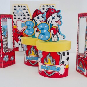 Puede incluir: Cajas de regalo rojas y negras con un perro d&aacute;lmata de dibujos animados que lleva un casco de bombero y sostiene una manguera de incendios. Las cajas tienen una ventana transparente y el texto "Matheo" en la parte delantera.