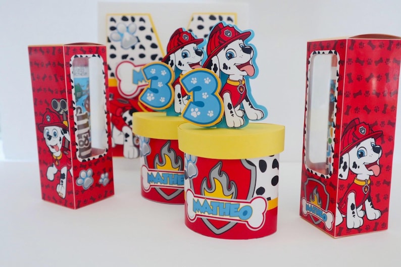 Puede incluir: Cajas de regalo rojas y negras con un perro d&aacute;lmata de dibujos animados que lleva un casco de bombero y sostiene una manguera de incendios. Las cajas tienen una ventana transparente y el texto "Matheo" en la parte delantera.