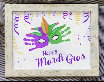 May include: A white framed canvas with a handprint art project depicting a purple and green Mardi Gras mask. The text "Happy Mardi Gras" is written in black cursive lettering below the mask.