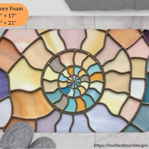 May include: A colorful bathroom rug with a stained glass design featuring a spiral pattern in shades of blue, yellow, pink, and purple. The rug is available in two sizes: 24 inches by 17 inches and 34 inches by 21 inches.
