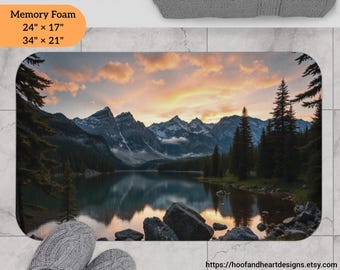 May include: A scenic bath mat featuring a mountain lake with a sunset sky and a reflection of the mountains in the water. The bath mat is available in two sizes: 24" x 17" and 34" x 21".