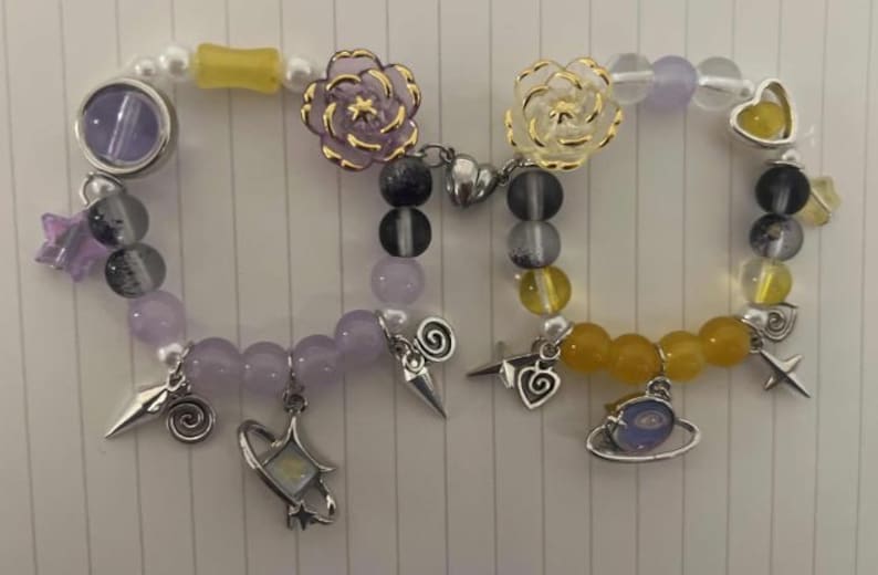 Pu&ograve; includere: Due braccialetti con perline viola e gialle, ciondoli e fiori. Un braccialetto ha un ciondolo a forma di fiore viola e l'altro ha un ciondolo a forma di fiore giallo.