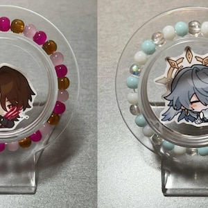 May include: Two bracelets with cartoon characters on them. The bracelet on the left has pink and brown beads. The bracelet on the right has blue and white beads.