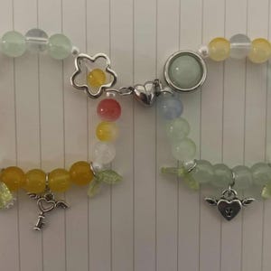 Pu&ograve; includere: Due braccialetti con perline color pastello e ciondoli. Un braccialetto ha un ciondolo a forma di fiore e un ciondolo a forma di chiave. L'altro braccialetto ha un ciondolo a forma di cuore e un ciondolo a forma di stella.