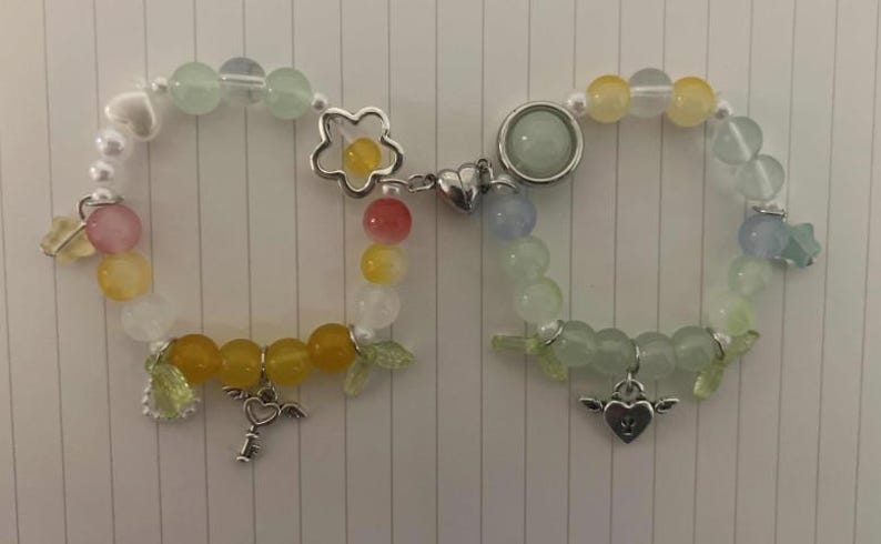 Pu&ograve; includere: Due braccialetti con perline color pastello e ciondoli. Un braccialetto ha un ciondolo a forma di fiore e un ciondolo a forma di chiave. L'altro braccialetto ha un ciondolo a forma di cuore e un ciondolo a forma di stella.