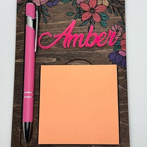 May include: A wooden desk organizer with a floral design, the name "Amber" engraved in pink, a pink pen, and a sticky note pad.