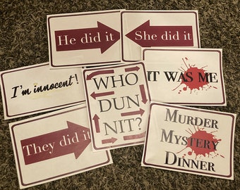 May include: A set of six signs for a murder mystery dinner party. The signs are white with red text and a red blood splatter design. The signs read: "He did it", "She did it", "I'm innocent", "Who Dunnit?", "It was me", and "Murder Mystery Dinner".
