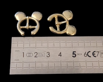 May include: Two gold-colored metal buckles with a Mickey Mouse head design. The buckles are approximately 2.5 cm wide and are measured against a ruler.