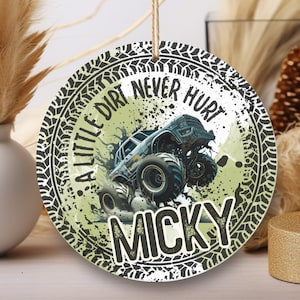 May include: A round, green and black ornament with a monster truck driving through mud. The ornament has a tire tread border and the text "A little dirt never hurt" and the name "Micky".