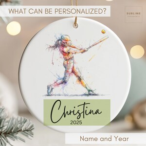 May include: White ceramic ornament featuring a watercolor illustration of a softball player swinging a bat. The ornament includes the name "Christina" and the year "2025" on a green rectangle. The text "What Can Be Personalized?" is at the top.
