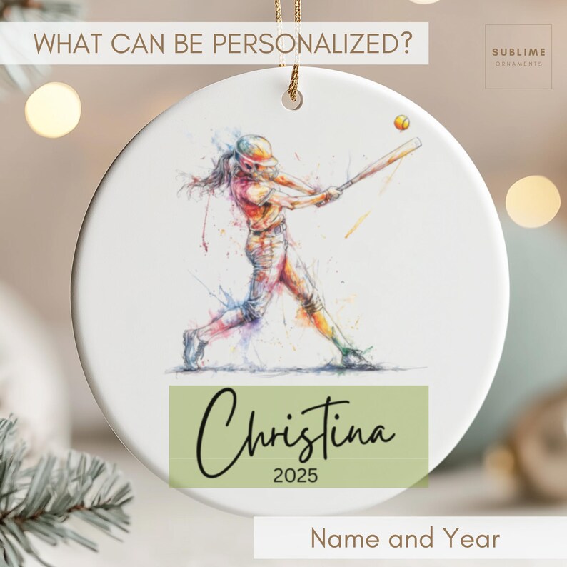 May include: White ceramic ornament featuring a watercolor illustration of a softball player swinging a bat. The ornament includes the name "Christina" and the year "2025" on a green rectangle. The text "What Can Be Personalized?" is at the top.