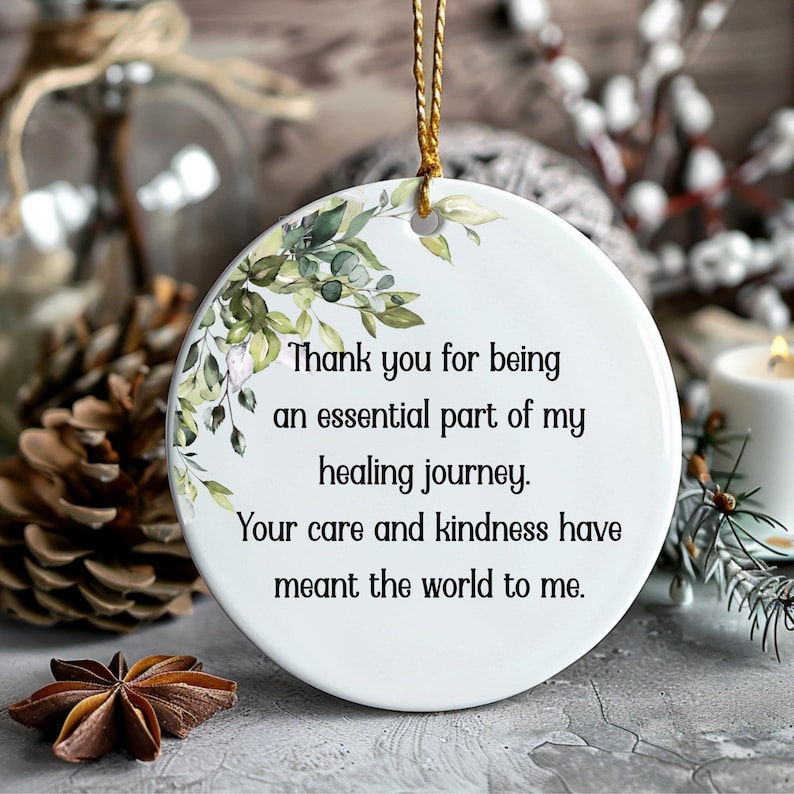 K&ouml;nnte beinhalten: Ein runder, wei&szlig;er Keramikschmuck mit einem goldenen Aufh&auml;ngeband. Er hat ein Blumendesign und den Text: "Danke, dass du ein wesentlicher Bestandteil meiner Heilungsreise bist. Deine F&uuml;rsorge und Freundlichkeit haben mir die Welt bedeutet."